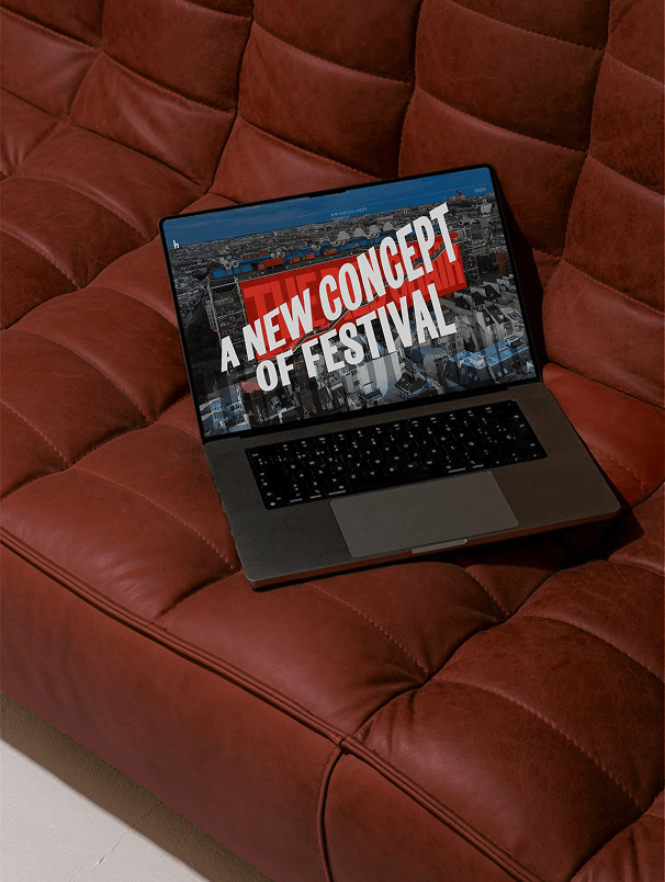 THE RED CHAIR — portátil sobre un sofá de cuero mostrando la web del festival