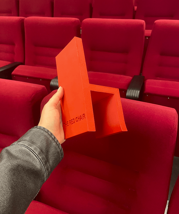 THE RED CHAIR — entrada de cartón en forma de silla roja en una sala de cine